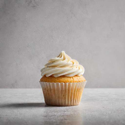 A white cupcake with a light brown frosting sits on a gray countertop against a plain gray wall backdrop.